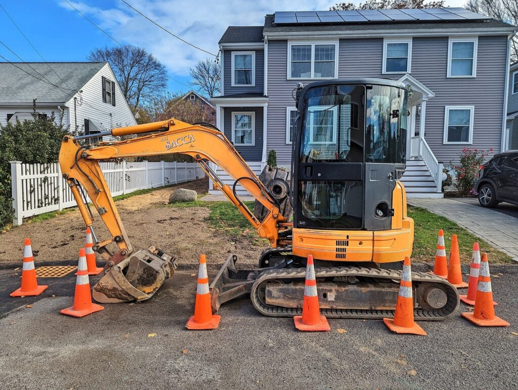 Orange traffic cones around a small excavator at a roadside work zone
